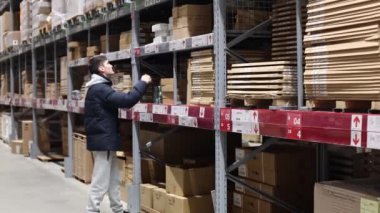Mavi ceketli yakışıklı beyaz bir adam, kış günü bir mağazada stokta üst raftan gelen mallarla dolu bir kutuyu çıkarıyor, yavaş çekimde yakın çekimde. Çevrimdışı alışveriş kavramı.