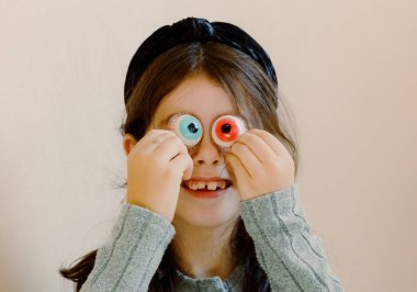 Portrait of one Caucasian beautiful cute girls with a black headband who creatively plays with Halloween candies, applying them to her eyes, on an autumn sunny morning, side view very close up. Happy clipart