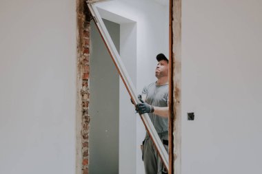 Üniformalı ve gri tekstil eldivenli genç beyaz bir adam bir tahtayı iki eliyle, seçici bir odak noktasıyla yan taraftan ayırıyor. İnşaat işi kavramı.