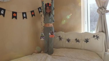 Beyaz tenli güzel bir kızın portresi yatağın üzerinde duruyor, asılı dekor gösteriyor, şarkı söylüyor ve kameraya doğru yürüyor, sonbahar sabahı yatak odasında güneş parlıyor, yakın.