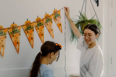 İki güzel Kafkasyalı mutlu kızın portresi mutfağı şenlikli turuncu Cadılar Bayramı bayraklarıyla süslüyor. Sonbahar günü, yakın çekimde, mutfaktaki duvarda. Zaman kavramı