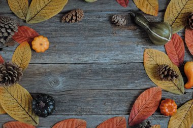 Sonbahar yapraklarından, kozalaklardan ve balkabaklarından oluşan ev yapımı güzel bir çelenk. Merkezinde fotokopi alanı bulunan eski bir ahşap kırsal masa üzerinde yuvarlak bir çerçevede duruyor.