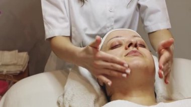 Tanımlanamayan genç bir kozmetik uzmanı parmaklarıyla boynuna ve çenesine masaj yapıyor. Güzellik salonundaki masaj masasında gözleri kapalı yatan bir müşteriye.