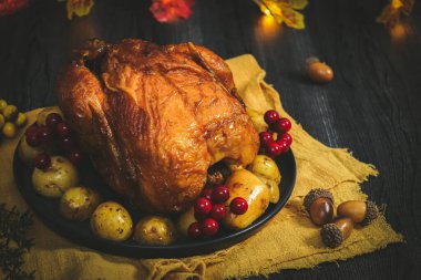 Sarı bir mutfak peçetesinde patatesli tavuk, siyah ahşap bir masada çelenk yaprakları ve meşe palamudu, yakın plan yan görüş..