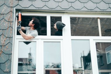 İki yakışıklı beyaz adam bir bahar günü plastik çerçevelerdeki çatlakları kapatmak için silikonlu bir silahla pencereyi tamir ediyor. Tamir için kavram ve