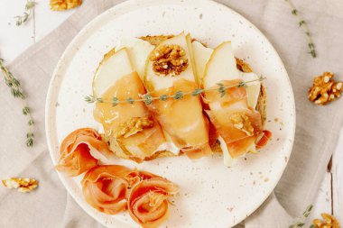 Armut, peynir, fındık, bal, kurutulmuş dilimler ve mısır gevreği ekmeğindeki bir dal biberiye beyaz ahşap bir masada peçetenin üzerinde duruyor.