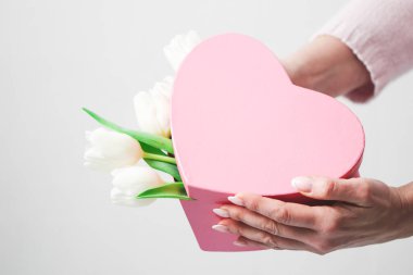 Üzerinde beyaz laleler olan pembe bir kutu beyaz bir kadının ellerinde beyaz bir duvara karşı güzel bir manikürle tarın derinliğine yakın bir açıdan bakan beyaz bir kadın. Sevgililer Günü kavramı