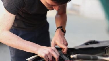 Bir genç, beyaz bir adam, bir arabanın kaputunda koruyucu bir kılıf altında arızaları onarıyor. Bir araba ampulünü değiştirme kavramı.