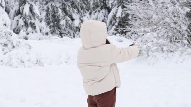 Beyaz puhrvik kapüşonlu beyaz ceketli genç beyaz beyaz bir kız, yarım bir virajda duruyor, Belçika 'nın kış ormanlarında bir cep telefonunda selfie çekiyor, yakın plan