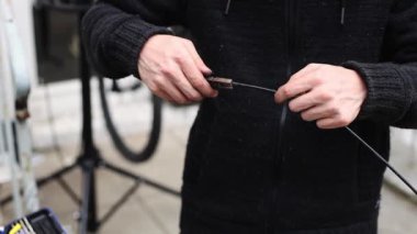 Genç bir beyaz adam pense takan bisiklet için fren kablolarından başlığı çıkartıyor, evin arka bahçesinde dikiliyor, yakından bakıyor. Bisiklet tamir konsepti.