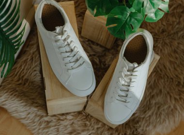 Bir çift güzel beyaz klasik spor ayakkabı ahşap sergi kutularının üzerinde duruyor. Kapıda duran doğal bir koyun derisi halı. Güneşli bir günde bir ev dükkanında, düz bir şekilde yatıyordu.