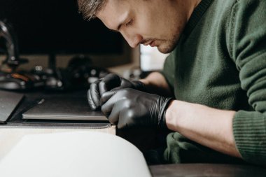 Siyah eldivenli yakışıklı beyaz bir adam dizüstü bilgisayarda koruyucu bir film seyrediyor, akşam bir ofis masasında, bir gece lambasının ışığı altında, yakın çekimde oturuyor.