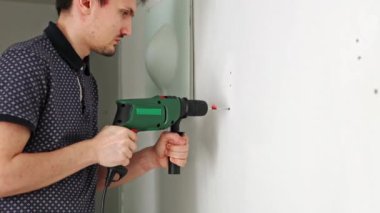 Genç, güzel, beyaz tenli esmer bir kadın iki eliyle matkabı tutuyor ve bir bahar günü odasına bir raf asmak için beyaz bir duvara yeni bir delik açıyor.