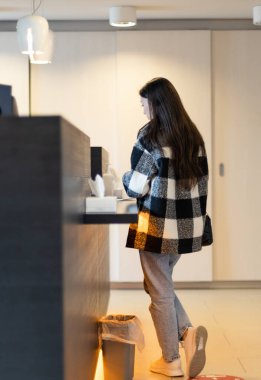 Ekose gömlekli, dalgalı saçlı, beyaz tenli bir kadın resepsiyon masasının arkasında diş hekimliği yapıyor..