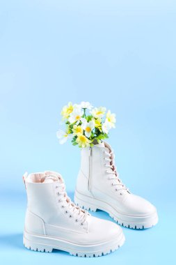 Beyaz yarı sezonluk eko-deriden yapılmış botlar, sert tabanlı, mavi arka planda bir buket bahar çiçeği, yakın plan yan görüş. Kadın ayakkabısı konsepti, bahar koleksiyonu.