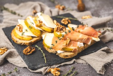 Armut, peynir, fındık, bal, kurutulmuş dilimler ve koyu çimento masadaki taş tepside biberiyeli bir çubuk biberiye, tarlanın derinliği ile yan görüş. Sağlıklı beslenme
