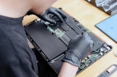 Siyah lateks eldivenli yakışıklı bir beyaz adam, bir yaz günü mutfaktaki masada otururken dizüstü bilgisayarın arkasını temizledikten sonra vantilatör takıyor.