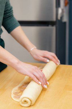 Tanınmayan genç beyaz bir kız kahverengi şeker ve tarçınlı hamuru ahşap bir masanın üstünde rulo içine yuvarlıyor, mutfakta duruyor, üstten yakından bakıyor. Pişirme için adım adım talimatlar
