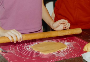 Tanımlanamayan beyaz bir kız masada duruyor ve yakın plan pembe silikon bir paspasın üzerinde duran ahşap bir oklavayla sarı ekmek hamuru yuvarlıyor. Adım adım talimatlar. Adım