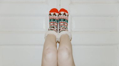 Yılbaşı çoraplı, tanınmayan genç beyaz bir kızın bacakları beyaz bir kapının önünde duruyor. Yan taraflarında fotokopi alanı var. Yeni Yıl 2025 kavramı, tatil zamanı