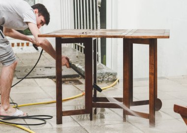 Gri eşofmanlı ve tişörtlü beyaz bir adam evinin arka bahçesindeki donmuş suyun basıncıyla ahşap bir bahçe masasını yıkıyor, aşağıdan manzara, yakın plan. Şey...