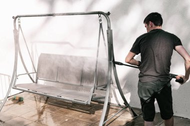 Siyah elbiseli esmer beyaz bir adamın portresi yalın ayak ayakta dikilip evinin arka bahçesinde salıncakta salıncak yıkarken basınçlı su püskürterek bir kercher, yakın plan