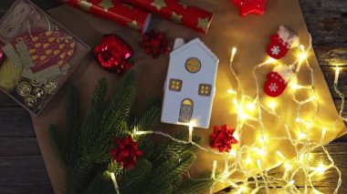 Beyaz porselen evin güzel atmosferik manzarası, yanan çelenk, kutu, iki rulo ambalaj kağıdı ve tatil süslemesi ahşap masa üzerindeki el işi kağıt peçetenin üzerinde, düz yatıyordu.