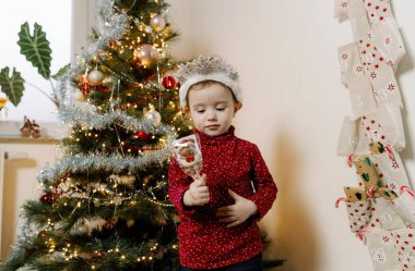 Beyaz kar taneleri tacı takmış küçük beyaz bir kız bir Noel ağacı ile gelişmekte olan takvimin arasında duruyor. Bir eliyle çikolatalı Noel Baba 'yı tutuyor ve bir gözünü kapıyor.