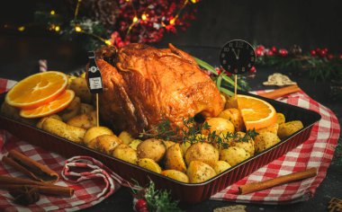 Patatesli tavuk, otlar, portakal ve kağıt saat gece yarısı fırın kabında bir şişe şampanya ve siyah arka planda yeni yıl süslemesi..