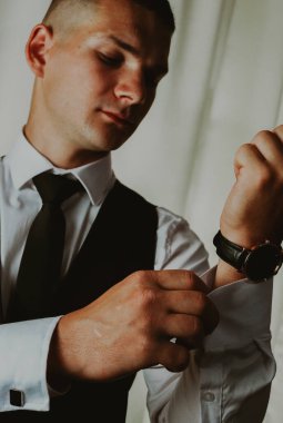 Siyah takım elbiseli beyaz bir damadın portresi. Gömlek koluna kol düğmeleri ilikli. Yaz sabahı odada duruyor. Damadın düğüne hazırlanması kavramı