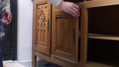 Genç bir Kafkasyalı teftiş eder ve sonra kapıyı onarmak ve boyamak için eski kahverengi ahşap bir dolabın menteşesinden manuel olarak kaldırır, seçici odaklı ve yavaş çekimde yan görüş. Yeni hayat