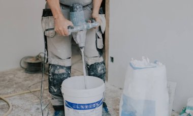 Beyaz macunu beyaz bir kovayla karıştıran beyaz tenli genç, beyaz bir erkek, kirli bir yerde, kapalı bir odada duruyor, üst tarafı kapalı, seçici bir odak noktası var. Şey...