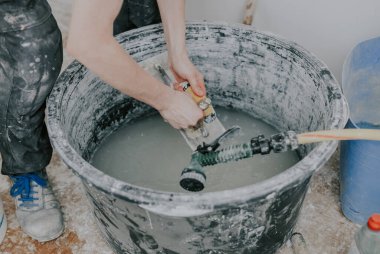 Siyah üniformalı genç beyaz bir adamın elleri, bir açıda duran, işi bitirdikten sonra, yakın çekimde, büyük siyah bir leğende bir fırça ve suyla spatula yıkar. İnşaat
