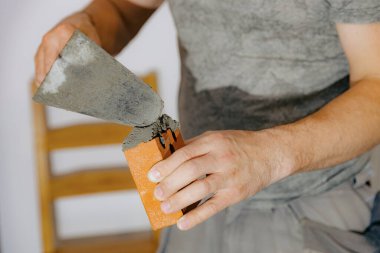 Tanınmayan genç bir beyaz adam, odadaki şöminenin şöminesinin bacası için bir mala kullanarak tuğlaya taze çimento harcı uyguluyor. Temiz tuğla işi kavramı