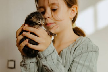 Güzel bir beyaz kız, yeni doğmuş küçük bir bebeği kucağında tutuyor. Bir klinikte beyaz bir duvarın önünde, bir ışık şeridi ile dikiliyor. Yan görünüşü çok yakın. Çocuk ve evcil hayvan kavramı
