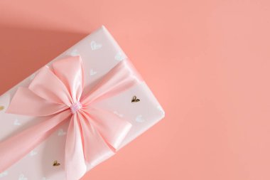 Solda fiyonklu güzel bir hediye kutusu var solda soluk pembe bir arka planda, sağda fotokopi alanı var, düz yakın plan..