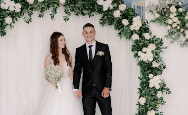 Güzel, mutlu ve gülen bir gelinin portresi bir buket beyaz yaka çiçeğiyle ve bir damat eşinin elini tutuyor ve bir yaz günü düğün salonunda ayakta duruyor.