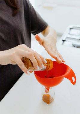 Tanınmayan genç bir beyaz kız, baharatlı spagetti baharatını eski bir kavanozdan yeni bir cam şeffaf kavanoza karıştırıyor ve yaz günü mutfakta beyaz bir masada duruyor.