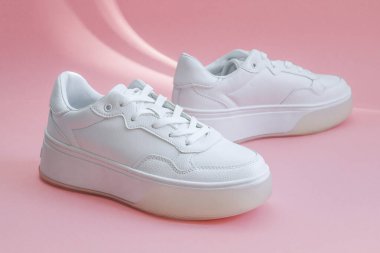 Bir çift beyaz spor ayakkabısı pembe arka plan görüntüsünün tam ortasında yatıyor. Moda, güzellik, ayakkabı konsepti.