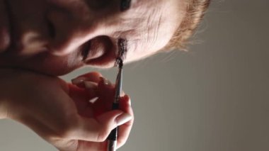 Genç bir beyaz kozmetik uzmanının eli, yaşlı bir kadın müşterinin gözleri kapalı bir şekilde akşam saatlerinde bir güzellik salonunda otururken sol kaşına koyu kahverengi boya sürüyor.