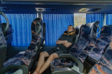 Gri takım elbiseli, boynunda yastığı olan, koridora doğru uzanmış, otobüste bir koltukta sessizce uyuyan, yol boyunca ilerleyen, yakın plan bir beyaz adam.