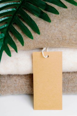 Boş bir kravat etiketi ve bir palmiye dalı düzgünce katlanmış beyaz bir rafta duran doğal yünden yapılmış üç parça ince gölgeli süveter.