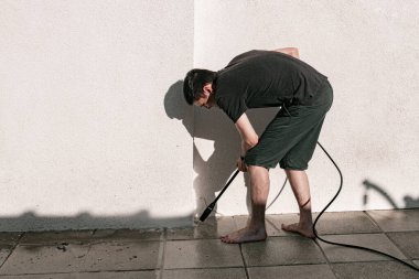 Beyaz adamın tam boy portresi. Kirli bahçe fayanslarını su jeti ile yıkıyor. Basınçlı çamaşır makinesiyle.