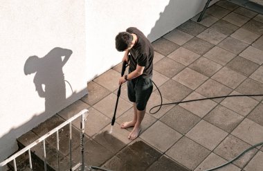 Beyaz adamın tam boy portresi. Kirli bahçe fayanslarını basınçlı su jeti ile yıkıyor. Basınçlı çamaşır makinesiyle.