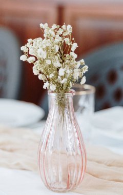 Aşağıdan yakın çekim manzarası olan bir şenlik masasında duran küçük pembe bir vazodaki küçük bir buket beyaz yaka çiçeğinin güzel manzarası. Parti zamanı konsepti, şenlikli dekorasyon.