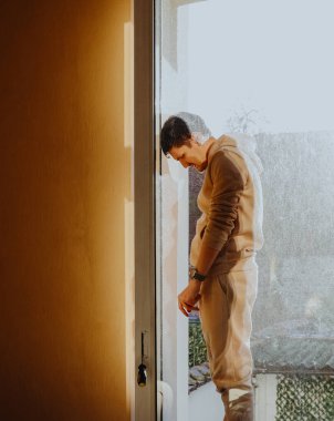Tadilata başlamadan önce güneşli bir günde açık bir odanın penceresinin dış penceresinden bakan beyaz bir adamın tam boy portresi, genel olarak yan görüş. Konsept:
