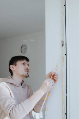 Bahar güneşli bir günde plastik bir pencere çerçevesinin iç kısmına içi boş bir plastik profil yapıştıran yakışıklı beyaz bir adamın bel boyunda portresi.