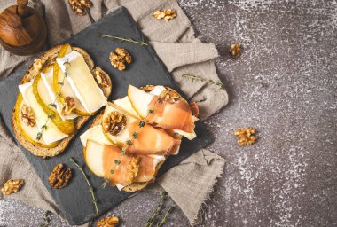 Armut, peynir, fındık, bal, kurutulmuş dilimler ve tahıllı ekmeğin üzerinde bir dal biberiye soldaki taş tepside koyu beton bir masada, düz bir şekilde uzanın. Sağlıklı yeme kavramı.