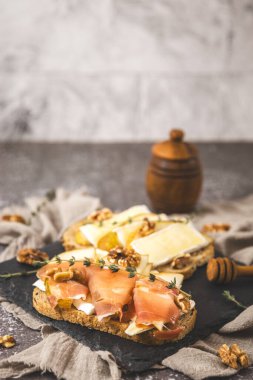 Armut, peynir, fındık, bal, kurutulmuş dilimler ve tahıllı ekmeğin üzerinde bir dal biberiye, koyu çimento masadaki taş tepside, tarlanın derinliğiyle yakın plan. Sağlıklı