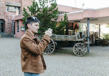 Tarihsel bir simgeyi cep telefonuyla çeken genç ve güzel bir esmer adamın portresi. Eski bir şatoda duruyor. Güneşli bir bahar günü.